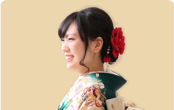 横顔で微笑む黒髪の女性。緑色の振袖を着て、髪飾りに赤い花を付けている華やかな和装姿。